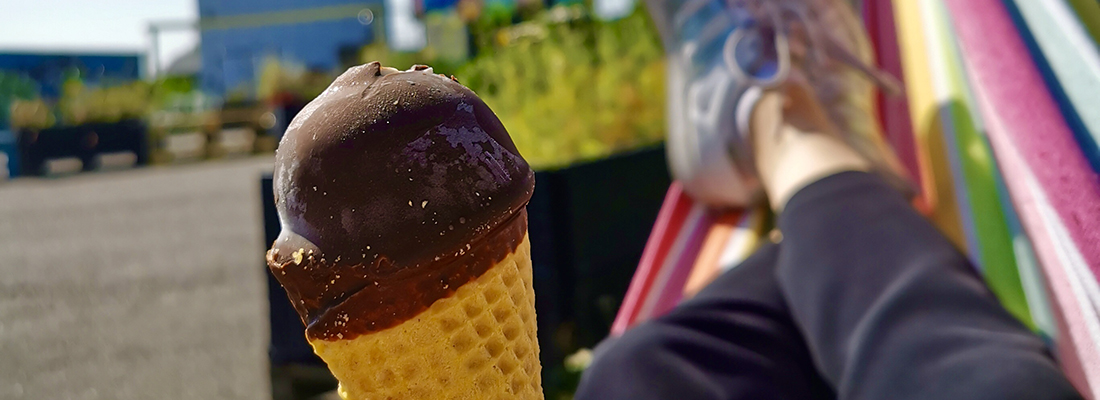 Närbild på glass med chokladöverdrag i strut. I bakgrunden syns delar av en person liggandes i hängmatta i starka färger.